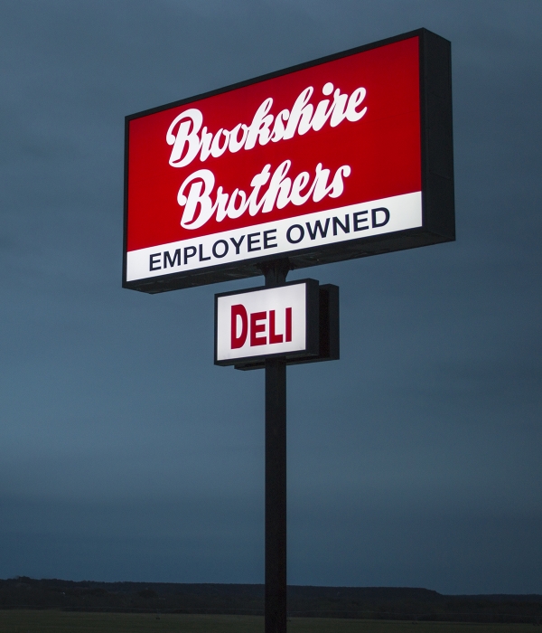 A Brookshire Brothers sign with "Employee Owned" and "Deli" callouts against the evening sky.