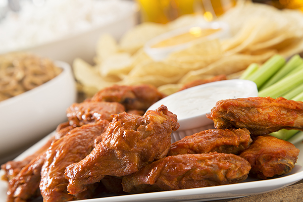 Hot wings, with pretzels, nachos, and beer in the background.