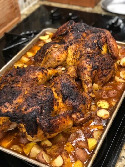 A roast chicken fresh out of oven, surrounded by potatoes and marinade