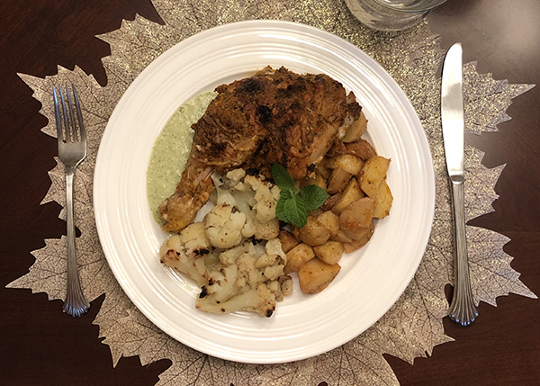 A shot looking down on a plate of roast chicken with vegetables and a green sauce, plated in a festive way.